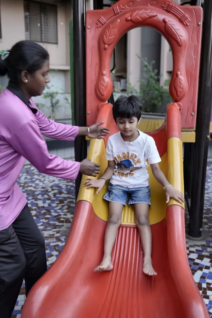Nanny supervising child at the playground slide